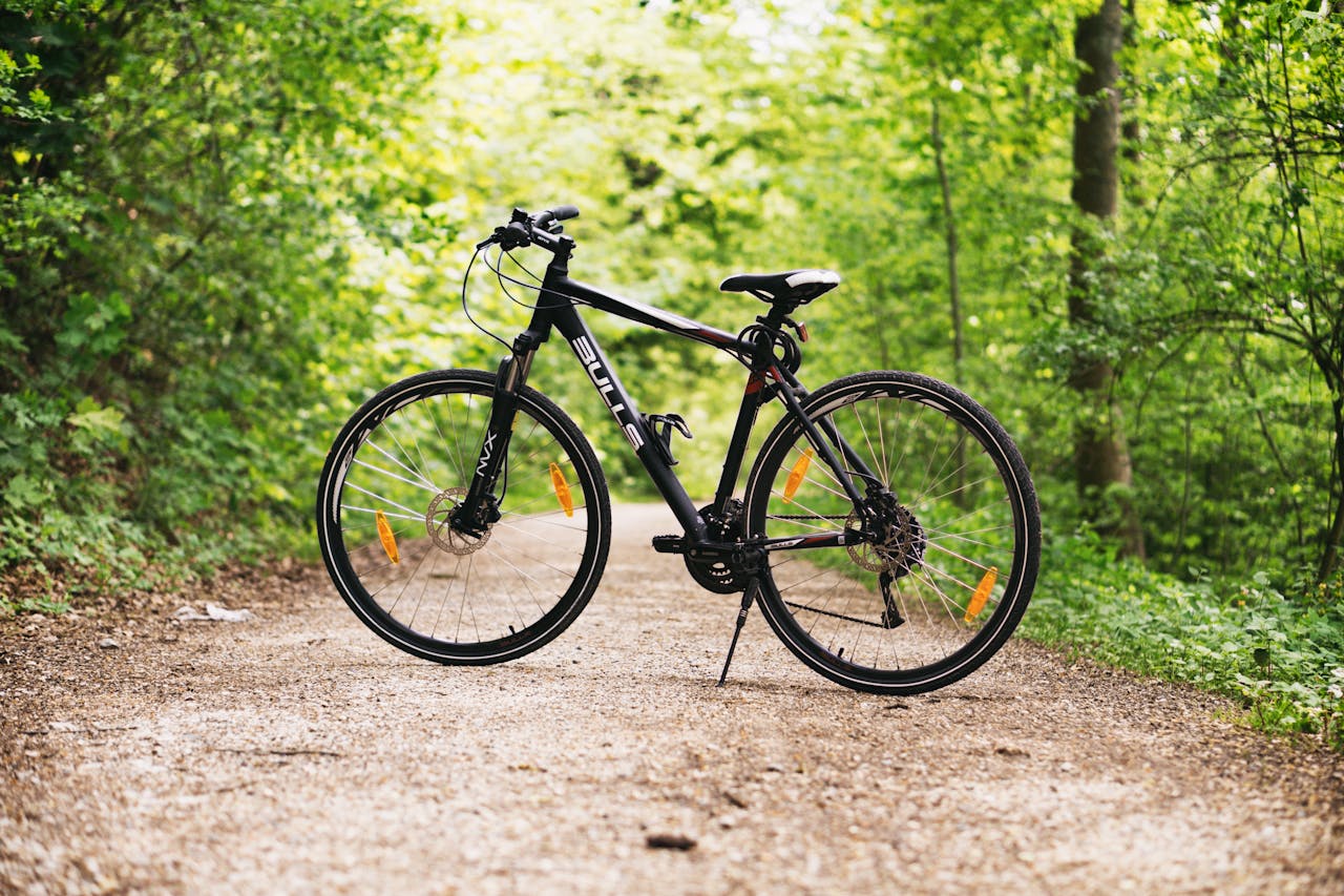 gallery-5 A mountain bike resting on a forest path surrounded by lush green trees in broad daylight.