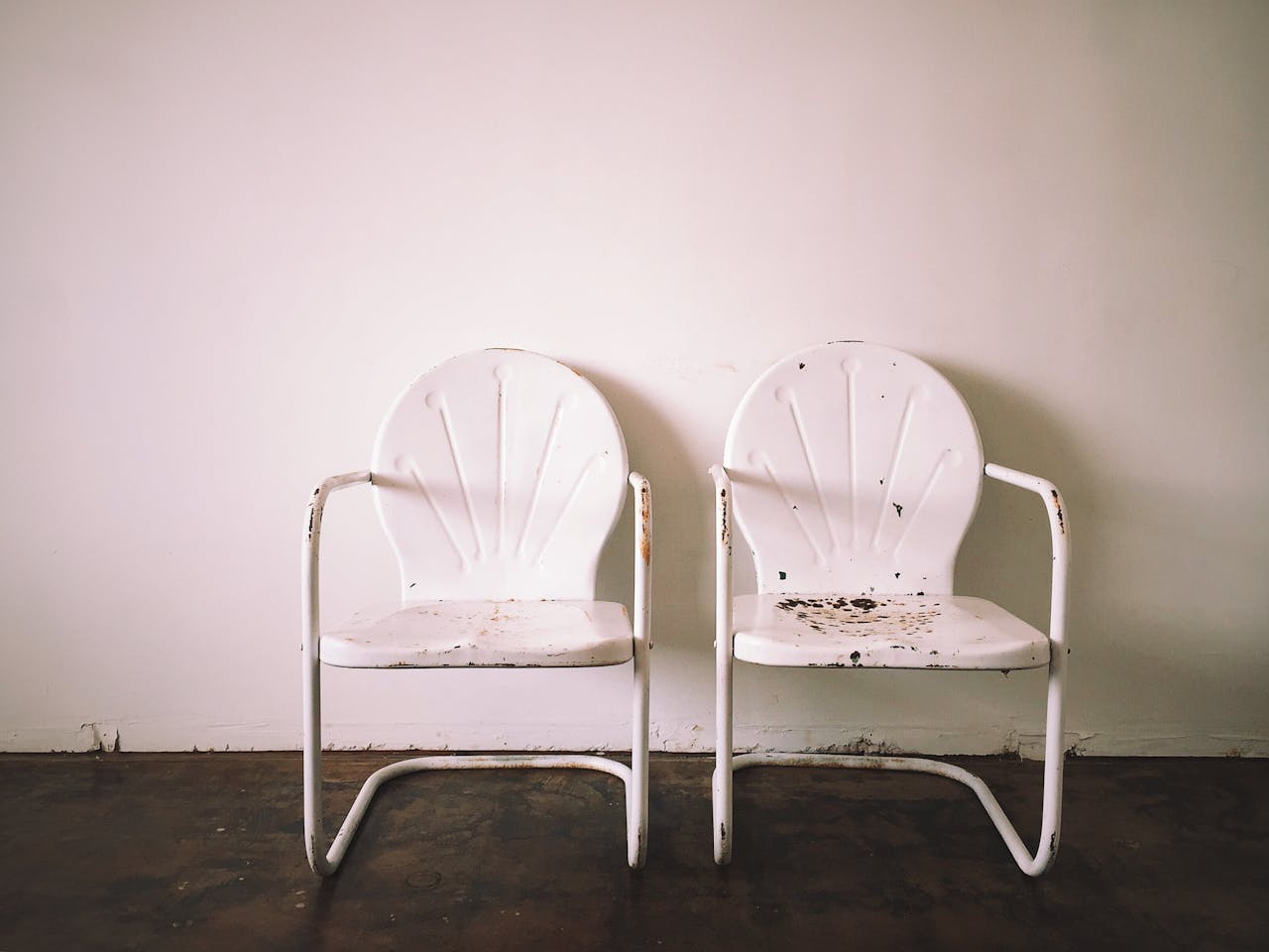 services-02 Two vintage white metal chairs against a bare wall, capturing minimalist aesthetics.