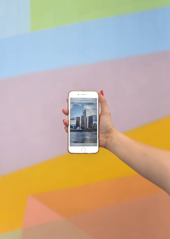 services-04 A hand holds a smartphone displaying a Detroit scene against a colorful wall.