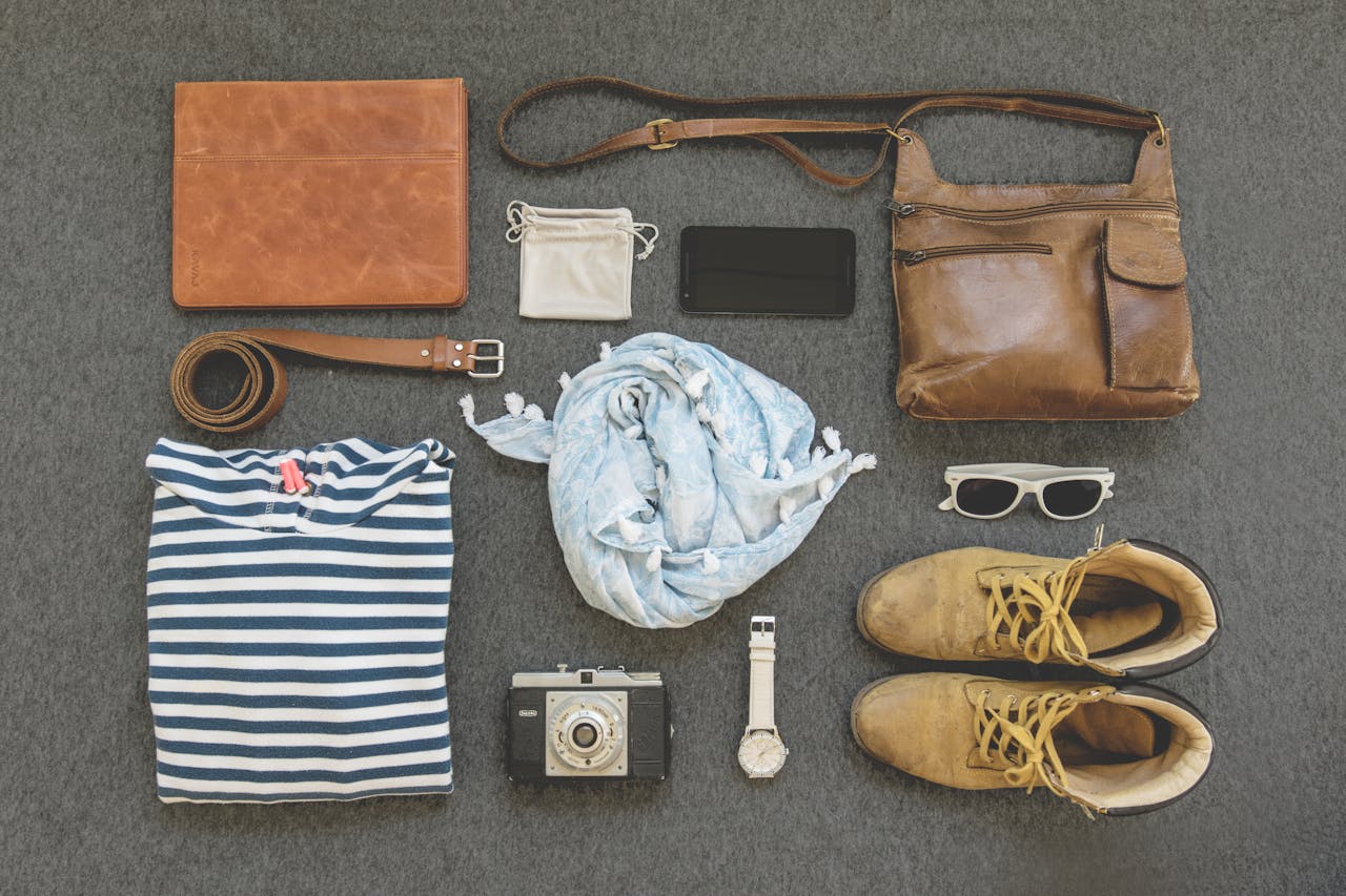 gallery-6 Vintage travel essentials flat lay with leather bags, shoes, camera, and clothing.