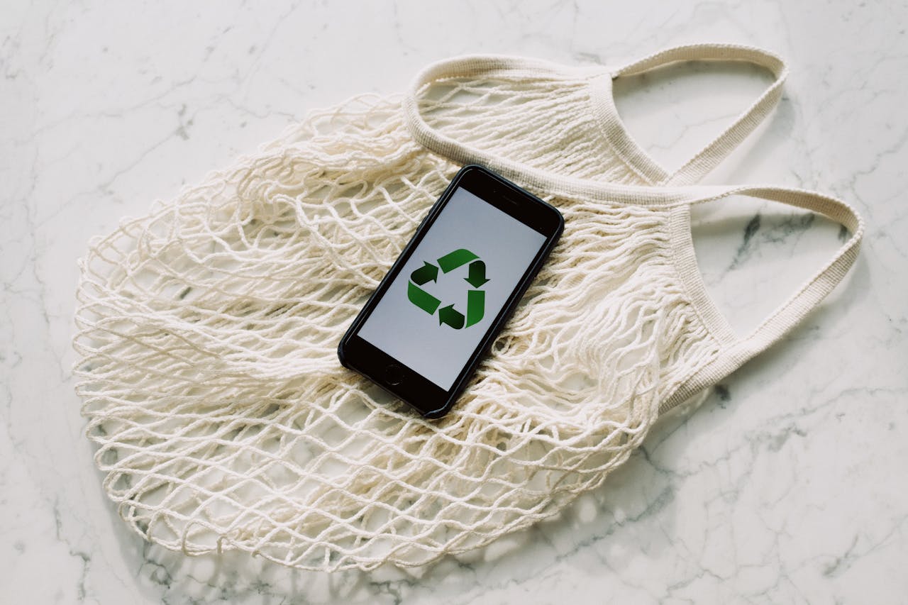 gallery-2 Overhead of smartphone with simple recycling sign on screen placed on white eco friendly mesh bag on marble table in room