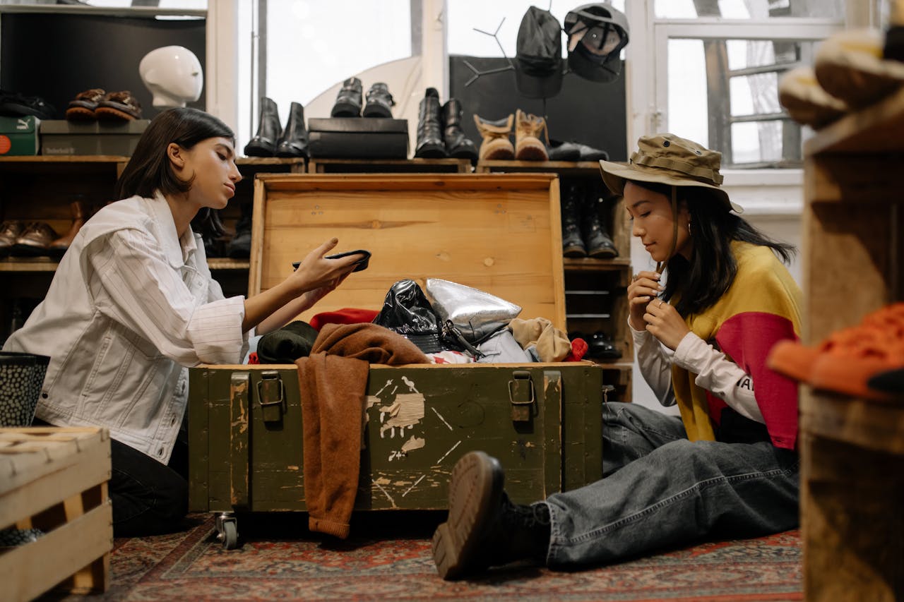 our-services-3 Two women exploring vintage fashion in a cozy thrift store, surrounded by clothes and shoes.