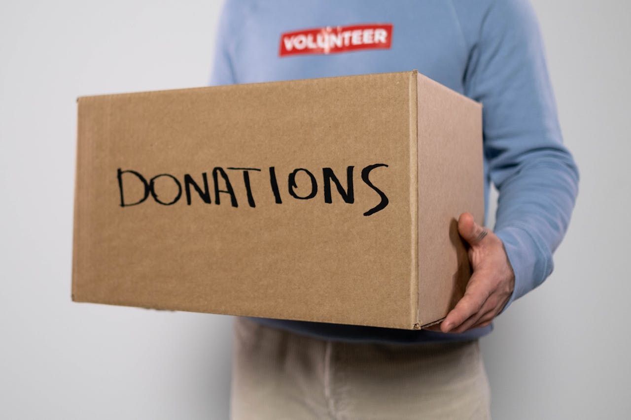 gallery-3 Close-up of a volunteer in a blue sweater holding a donation box. Concept of charity and volunteerism.