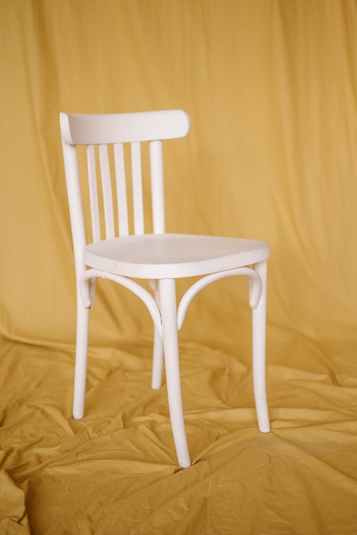 hero-img-01 White wooden chair against a soft mustard backdrop in a minimalist studio setting.